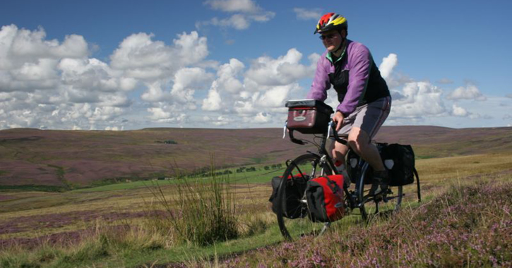 man cycling through the heather clad moorland of the North Pennines and Durham Dales.